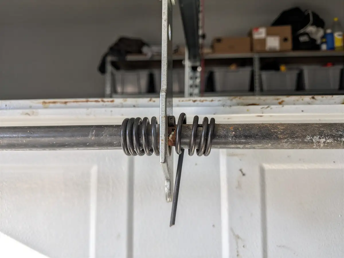 A close-up shows a garage door torsion spring on a metal shaft.